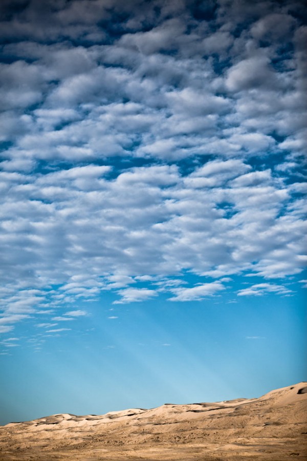 Sun beams shine through the desert clouds at Kelso Dunes